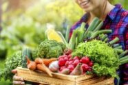 Frau hält Holzkiste mit Salat, Radieschen und anderem Gemüse