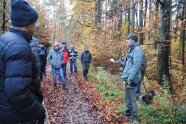 Mehrere Personen im Wald stehen im Halbkreis um einen Mann in Forstkleidung