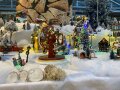 Miniatur-Figuren, -Häuser und -Fahrgeschäfte in winterlicher Landschaft.