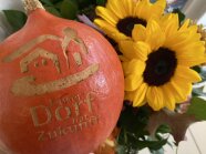 Kürbis mit eingraviertem "Unser Dorf"-Logo vor buntem Herbstblumenstrauß