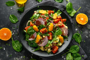 Teller mit gemischtem Salat, daneben Spinatblätter und zwei Orangenhälften 
